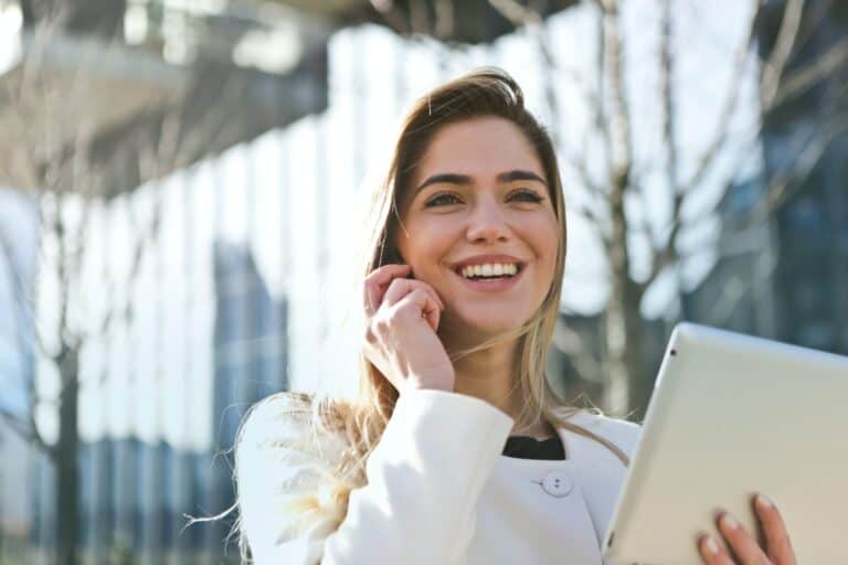 Smilende kvinne med nettbrett snakker i mobiltelefon utenfor et kontorbygg
