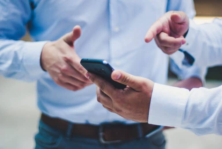 To kolleger i lyseblå skjorter ser på en mobiltelefon