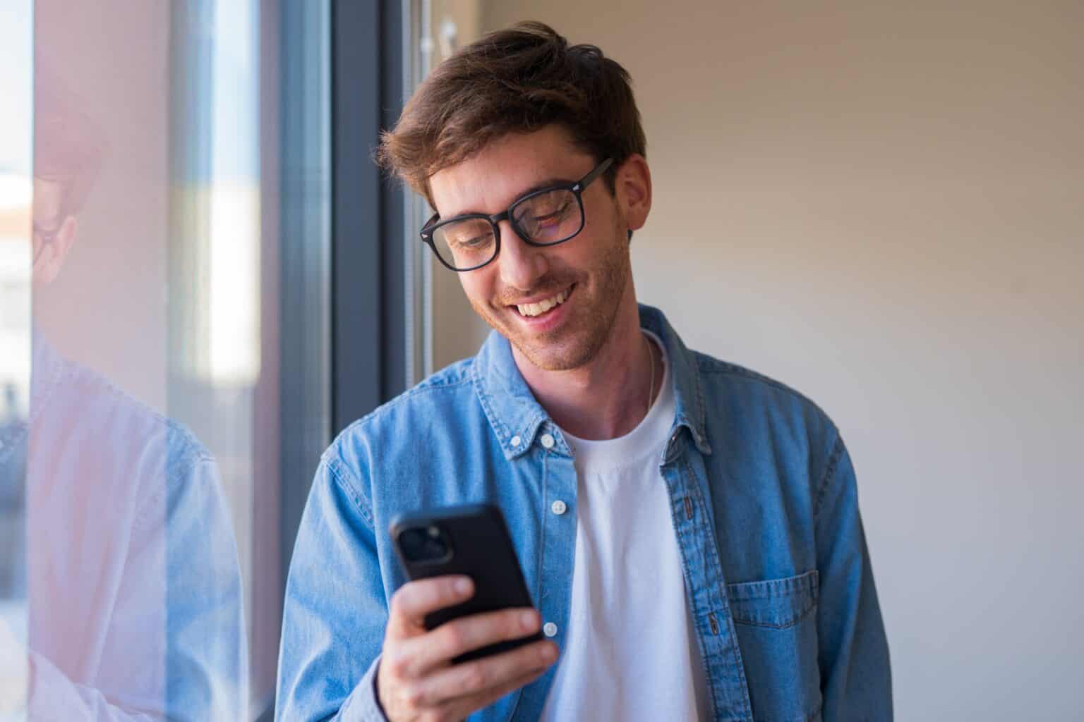 Fornøyd mann ser på smarttelefonen ved kontorvindu