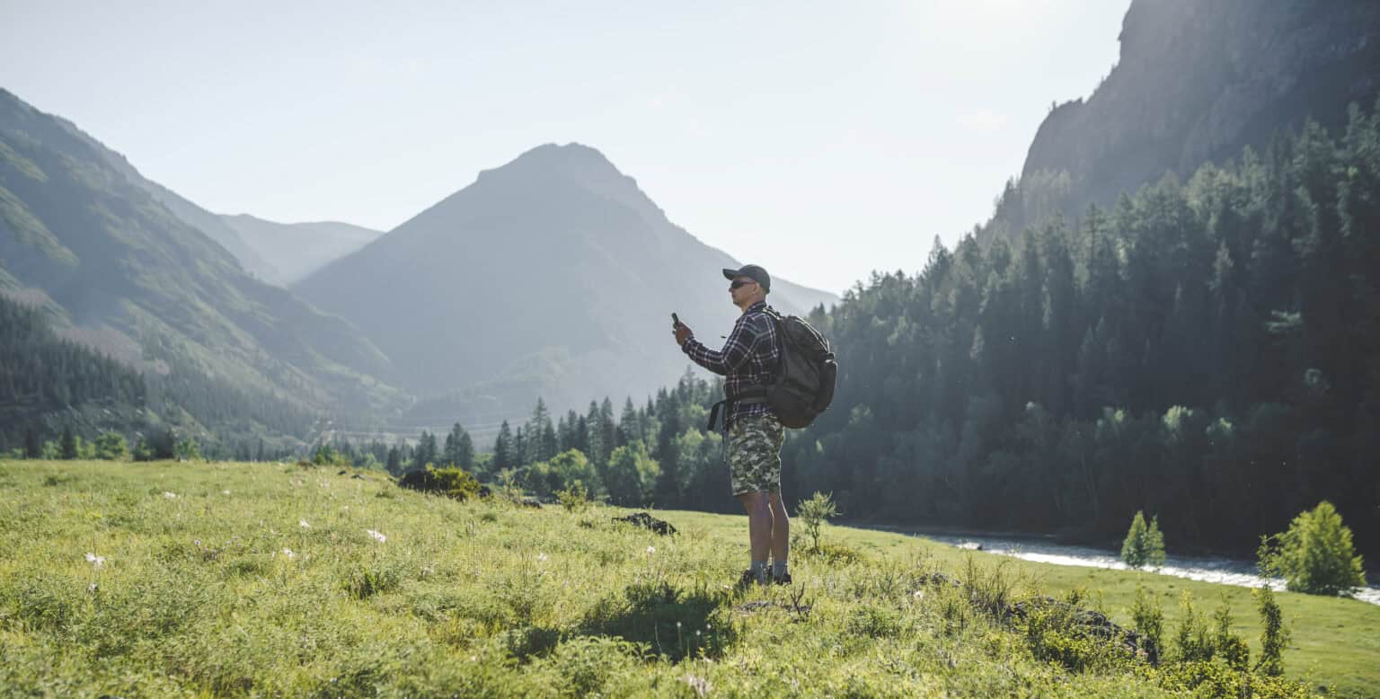 Mann sjekker mobiltelefonen i norsk fjellandskap