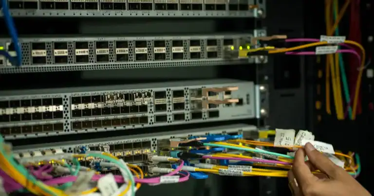 Hånd kobler fiberkabler i et patchepanel i et nettverksskap