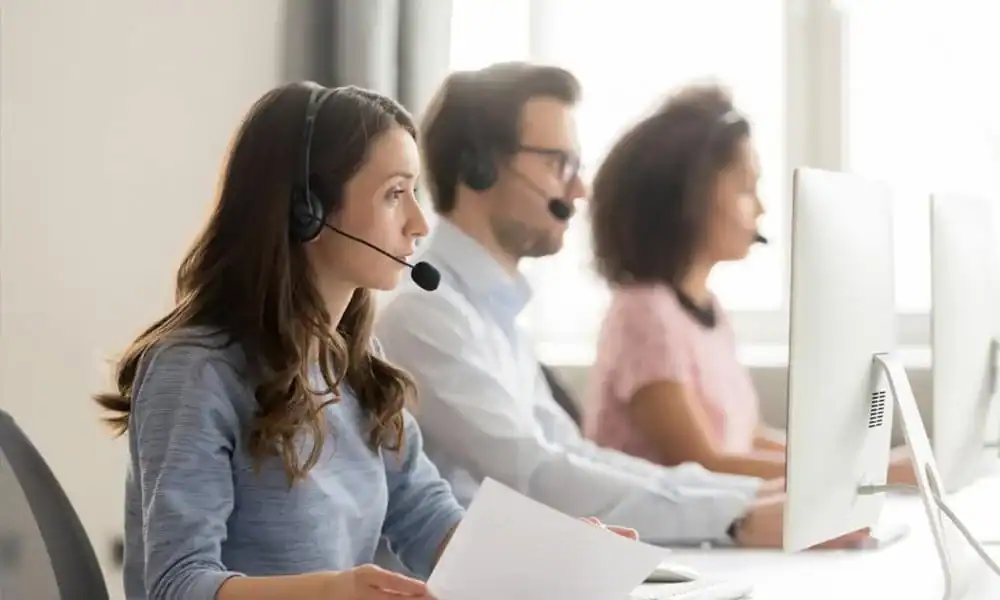Kundeservicemedarbeidere med hodesett svarer på telefon foran skjermene sine
