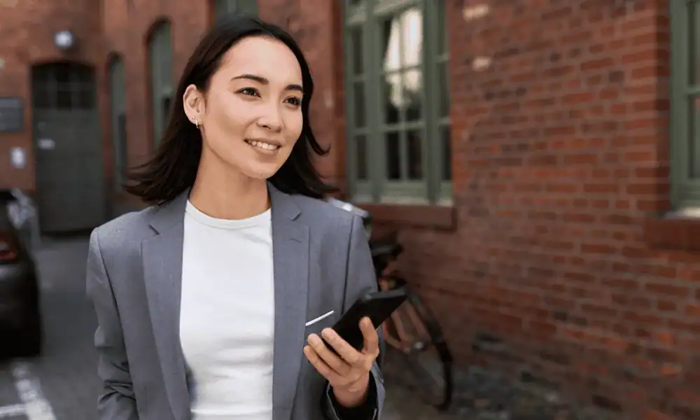 Kvinne i dressjakke ser på mobilen utenfor et kontorbygg